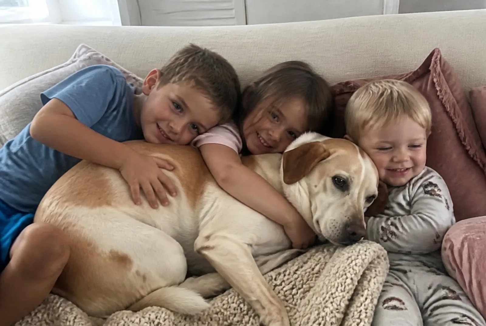 Unsere drei Kinder kuscheln mit dem Familienhund auf dem hellen Sofa